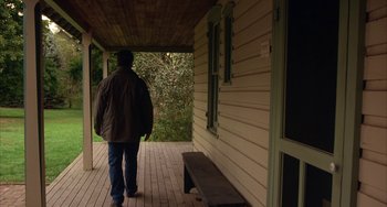 Movie still from “Signs” (2002), directed by M. Night Shyamalan – A person walking on a porch with a bench; Wide shot, Low angle