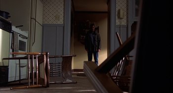 Movie still from “Signs” (2002), directed by M. Night Shyamalan – A person standing in a room with chairs and a table; Wide shot, High angle