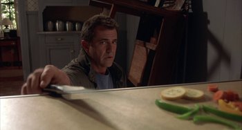 Movie still from “Signs” (2002), directed by M. Night Shyamalan – A man sitting in front of a counter holding a knife in his hand; Close Up shot, Low angle