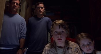 Movie still from “Signs” (2002), directed by M. Night Shyamalan – A young boy and a young man in a dark room; Medium shot, Low angle