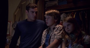 Movie still from “Signs” (2002), directed by M. Night Shyamalan – A man and two young children standing next to each other in a room; Medium shot, Over the shoulder angle