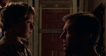 Movie still from “Signs” (2002), directed by M. Night Shyamalan – A man and a boy face each other in a dark room; Close Up shot, Over the shoulder angle