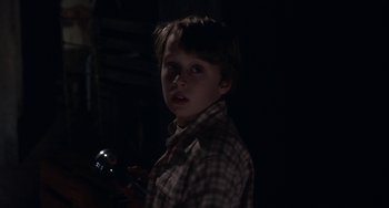 Movie still from “Signs” (2002), directed by M. Night Shyamalan – A young boy is standing in a dark room; Medium shot, High angle