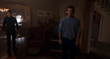 Movie still from “Signs” (2002), directed by M. Night Shyamalan – A man standing in a living room in front of a chair; Wide shot, Over the shoulder angle