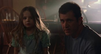 Movie still from “Signs” (2002), directed by M. Night Shyamalan – A man and a little girl standing next to each other; Close Up shot, Over the shoulder angle