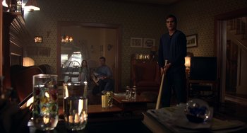 Movie still from “Signs” (2002), directed by M. Night Shyamalan – A man holding a baseball bat while standing in a living room; Wide shot, Over the shoulder angle