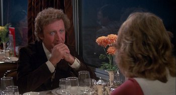 Movie still from “Silver Streak” (1976), directed by Arthur Hiller – A man sitting at a dinner table with a glass of wine; Medium shot, Over the shoulder angle