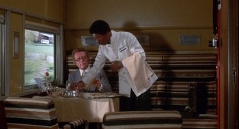 Movie still from “Silver Streak” (1976), directed by Arthur Hiller – A man standing at a table in front of another man; Medium shot, High angle