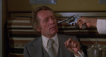 Movie still from “Silver Streak” (1976), directed by Arthur Hiller – A man in a suit and tie holding a gun up to his eye; Close Up shot, Over the shoulder angle