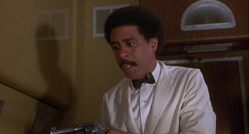 Movie still from “Silver Streak” (1976), directed by Arthur Hiller – A man in a white suit holding a gun in a room; Close Up shot, Low angle