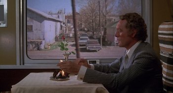 Movie still from “Silver Streak” (1976), directed by Arthur Hiller – A man sitting at a table with a cake on top of it; Medium shot, Over the shoulder angle