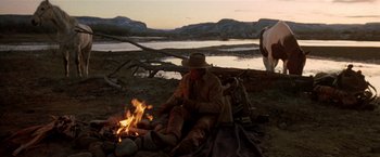 Movie still from “Silverado” (1985), directed by Lawrence Kasdan – A man sitting next to a fire on the ground; Wide shot, Low angle