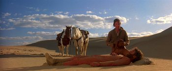 Movie still from “Silverado” (1985), directed by Lawrence Kasdan – A man standing next to two horses in the desert; Wide shot, Low angle