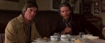 Movie still from “Silverado” (1985), directed by Lawrence Kasdan – Two men sitting at a table with a plate of food in front of them; Close Up shot, Low angle