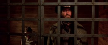 Movie still from “Silverado” (1985), directed by Lawrence Kasdan – A man with a beard and a cowboy hat behind a metal fence; Medium shot, Low angle