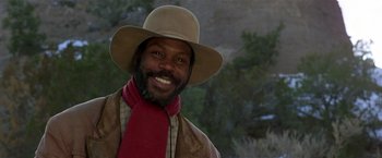 Movie still from “Silverado” (1985), directed by Lawrence Kasdan – A man wearing a cowboy hat and a scarf smiling; Close Up shot, Low angle