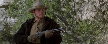 Movie still from “Silverado” (1985), directed by Lawrence Kasdan – A man holding a rifle in a wooded area; Medium shot, Low angle