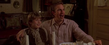 Movie still from “Silverado” (1985), directed by Lawrence Kasdan – A man and a boy sitting at a table with a cake in front of them; Medium shot, Over the shoulder angle