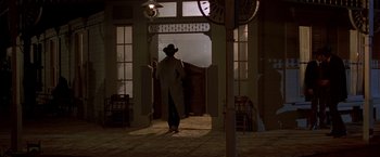 Movie still from “Silverado” (1985), directed by Lawrence Kasdan – A man in a hat standing in front of an open door; Wide shot, Low angle