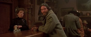 Movie still from “Silverado” (1985), directed by Lawrence Kasdan – A man sitting at a table with a glass of whiskey; Medium shot, Over the shoulder angle