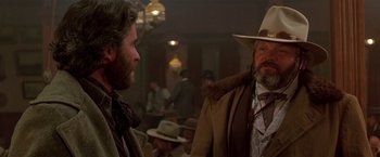 Movie still from “Silverado” (1985), directed by Lawrence Kasdan – Two men are talking to each other in a room; Medium shot, Over the shoulder angle