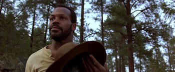 Movie still from “Silverado” (1985), directed by Lawrence Kasdan – A man holding a hat in a forest; Close Up shot, Low angle