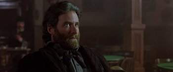 Movie still from “Silverado” (1985), directed by Lawrence Kasdan – A man with long hair and a beard sitting in a chair; Close Up shot, Low angle