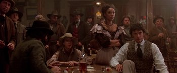 Movie still from “Silverado” (1985), directed by Lawrence Kasdan – A group of people sitting at a table with drinks; Medium shot, Over the shoulder angle