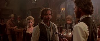 Movie still from “Silverado” (1985), directed by Lawrence Kasdan – A man with a gun in front of two other people; Medium shot, Over the shoulder angle