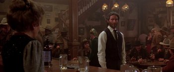 Movie still from “Silverado” (1985), directed by Lawrence Kasdan – A man standing at a bar with a hat on; Medium shot, Low angle