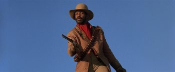 Movie still from “Silverado” (1985), directed by Lawrence Kasdan – A man holding a gun while wearing a hat; Medium shot, Low angle