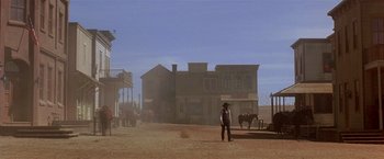 Movie still from “Silverado” (1985), directed by Lawrence Kasdan – A man standing in front of an old western town; Extreme Wide shot, Low angle