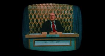 Movie still from “Sisters” (1972), directed by Brian De Palma – A man sitting at a table in front of a television; Medium shot, High angle