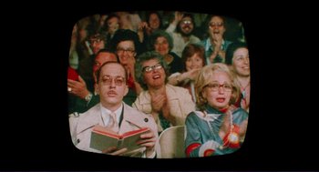 Movie still from “Sisters” (1972), directed by Brian De Palma – A group of people sitting and standing in a room; Medium shot, Over the shoulder angle