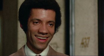 Movie still from “Sisters” (1972), directed by Brian De Palma – A person wearing a suit and tie smiling; Close Up shot, High angle