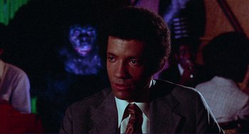 Movie still from “Sisters” (1972), directed by Brian De Palma – A man wearing a suit and tie in front of a crowd; Close Up shot, Low angle