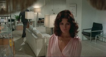 Movie still from “Sisters” (1972), directed by Brian De Palma – A woman in a pink dress standing in front of a white couch; Medium shot, Over the shoulder angle