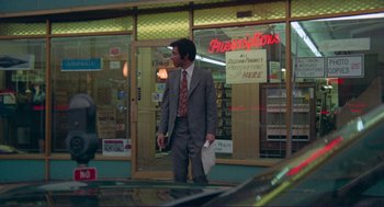 Movie still from “Sisters” (1972), directed by Brian De Palma – A man in a suit and tie walking in front of a store; Wide shot, Low angle