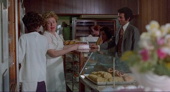 Movie still from “Sisters” (1972), directed by Brian De Palma – A woman serving a cake to a man in a suit; Medium shot, Over the shoulder angle