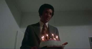 Movie still from “Sisters” (1972), directed by Brian De Palma – A man in a suit holding a birthday cake with lit candles on it; Medium shot, High angle