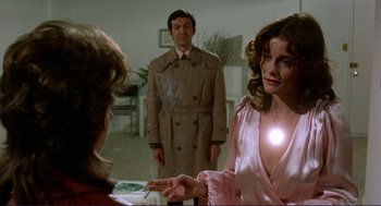 Movie still from “Sisters” (1972), directed by Brian De Palma – A woman in a trench coat is smoking a cigarette while a man in a trench coat looks on; Medium shot, Over the shoulder angle