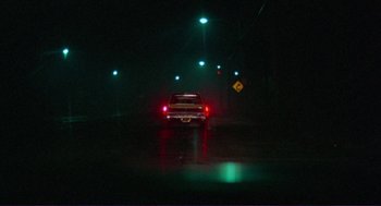 Movie still from “Sisters” (1972), directed by Brian De Palma – A car driving down a street at night with green lights; Extreme Wide shot, High angle