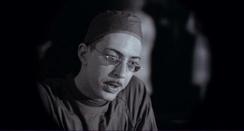 Movie still from “Sisters” (1972), directed by Brian De Palma – A black and white photo of a man wearing glasses and a hat; Close Up shot, Low angle