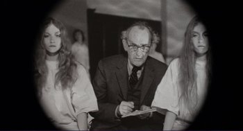 Movie still from “Sisters” (1972), directed by Brian De Palma – An older man sitting in front of two young women; Medium shot, Over the shoulder angle