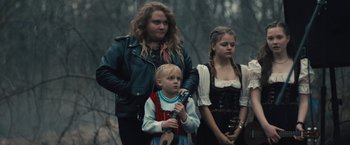 Movie still from “Skin” (2018), directed by Guy Nattiv – A woman standing next to a child holding a guitar; Medium shot, Over the shoulder angle