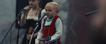 Movie still from “Skin” (2018), directed by Guy Nattiv – A young girl in a red and white dress is holding a microphone; Close Up shot, Over the shoulder angle