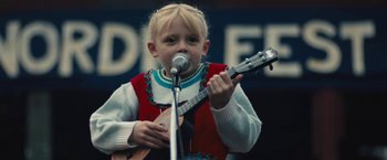 A little girl holding a guitar while standing at a microphone