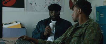 Movie still from “Skin” (2018), directed by Guy Nattiv – A man holding a coffee cup while sitting next to another man; Medium shot, Over the shoulder angle