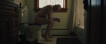 Movie still from “Skin” (2018), directed by Guy Nattiv – A naked man sitting on top of a white toilet seat; Medium shot, High angle