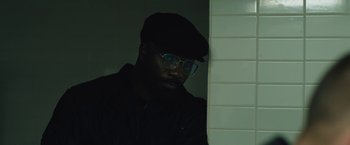 Movie still from “Skin” (2018), directed by Guy Nattiv – A man wearing glasses and a hat is standing by a wall; Close Up shot, Low angle